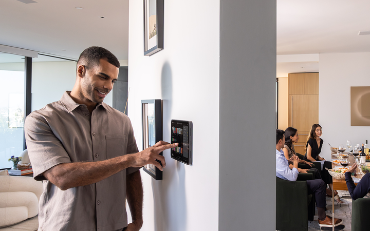 Homeowner controls music from a wall-mounted iPad in an IPORT mount while guests dine in the next room