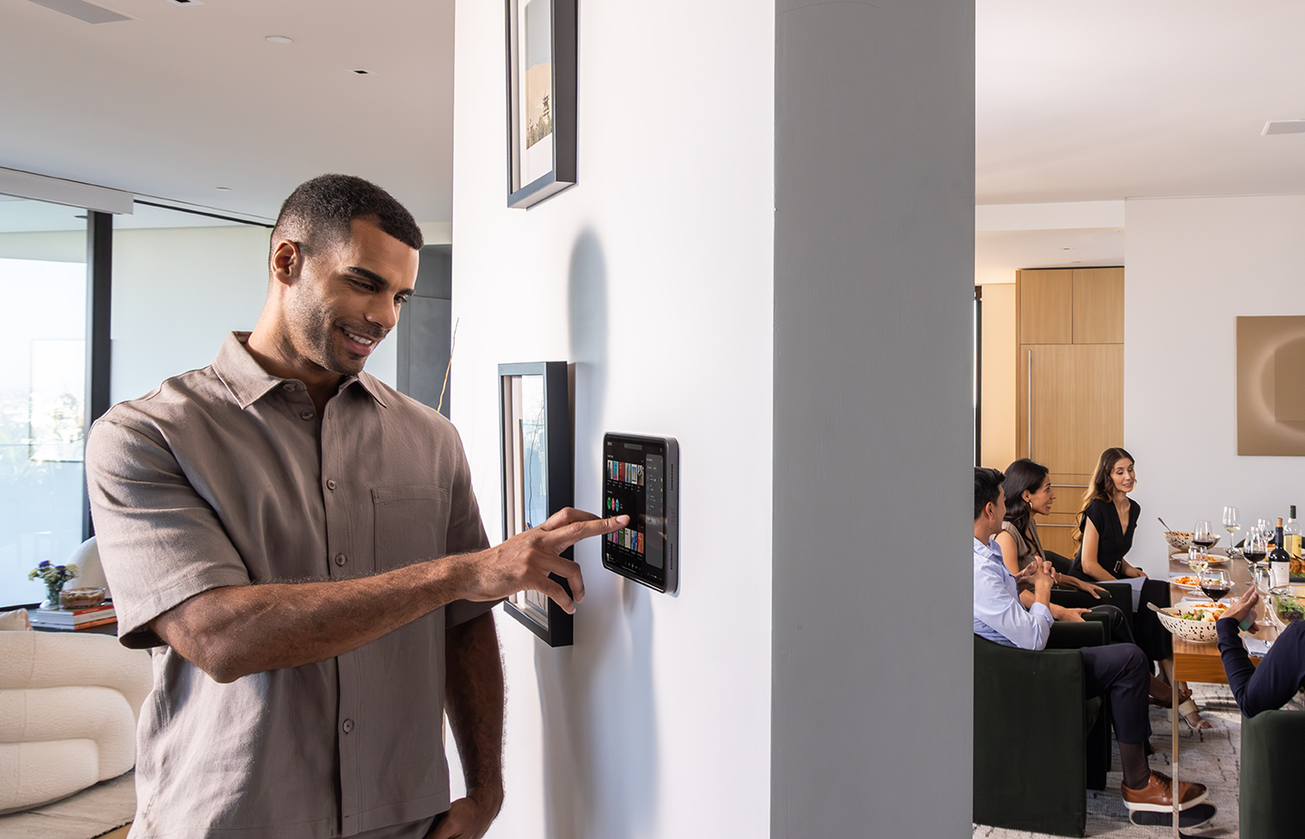 Homeowner controls music from a wall-mounted iPad in an IPORT mount while guests dine in the next room